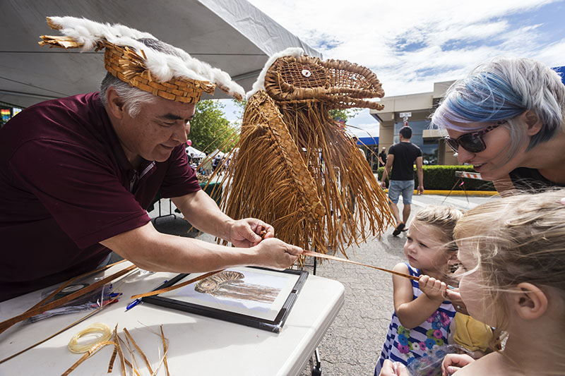 Indigenous artist demonstrating traditional cedar weaving to children at community market